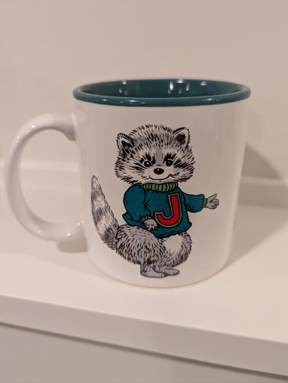 White Ceramic Mug with Teal Interior and Playful Joy Raccoon Design